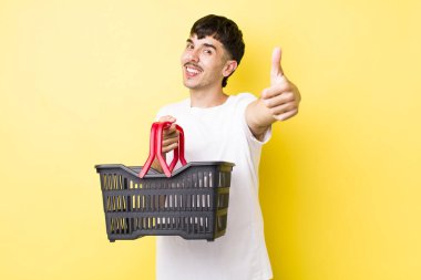 Genç İspanyol adam gururlu, olumlu bir şekilde gülümsüyor. boş alışveriş sepeti kavramı