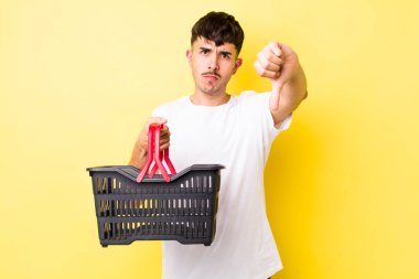 Genç, Latin asıllı, kızgın, baş parmağını kaldırmış. boş alışveriş sepeti kavramı