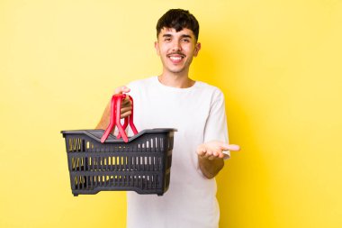 Genç İspanyol adam mutlu bir şekilde gülümsüyor ve bir konsept sunuyor. boş alışveriş sepeti kavramı