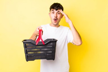 Genç İspanyol adam mutlu, şaşkın ve şaşırmış görünüyor. boş alışveriş sepeti kavramı