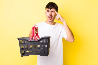 Genç İspanyol adam şaşkın ve şaşkın hissediyor, senin deli olduğunu gösteriyor. boş alışveriş sepeti kavramı