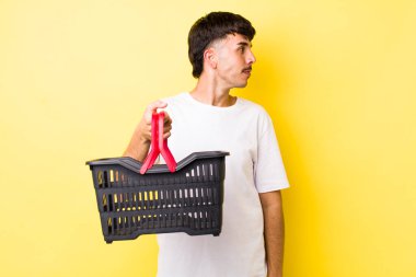 Profil görünümlü genç İspanyol adam hayal mi kuruyor, hayal mi kuruyor yoksa hayal mi kuruyor? boş alışveriş sepeti kavramı