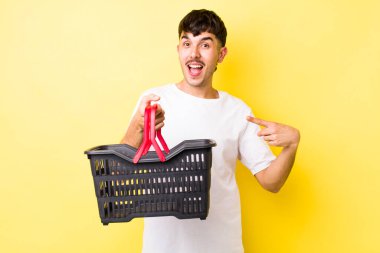 Genç İspanyol adam heyecanlı ve şaşırmış görünüyor. boş alışveriş sepeti kavramı
