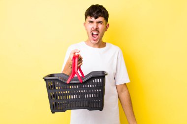 Genç İspanyol adam agresif bir şekilde bağırıyor, çok kızgın görünüyor. boş alışveriş sepeti kavramı