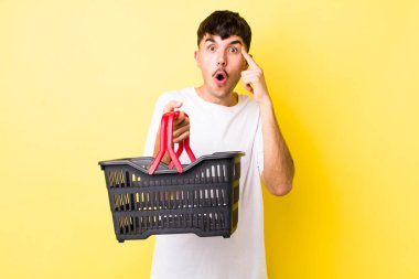 Genç İspanyol adam şaşırmış görünüyor, yeni bir düşünce, fikir ya da konsept keşfediyor. boş alışveriş sepeti kavramı