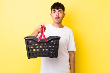 Genç İspanyol adam şaşkın ve şaşkın görünüyor. boş alışveriş sepeti kavramı