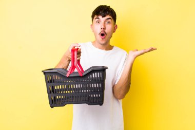 Genç İspanyol bir adam şaşırmış ve şok olmuş görünüyor. Çenesi düşmüş ve elinde bir nesne tutuyor. boş alışveriş sepeti kavramı