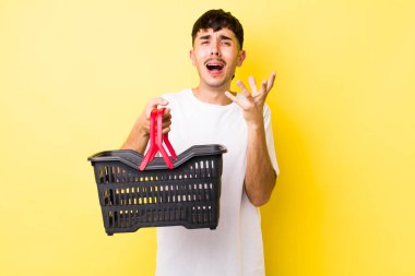 Genç İspanyol adam umutsuz, hayal kırıklığına uğramış ve stresli görünüyor. boş alışveriş sepeti kavramı