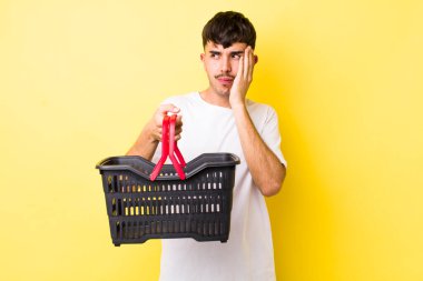 Genç İspanyol bir adam bıkkın, bezgin ve uykulu hissediyor. boş alışveriş sepeti kavramı