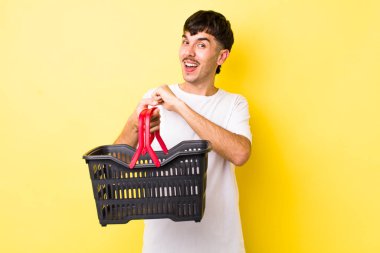 Genç İspanyol adam kendini mutlu hissediyor ve bir meydan okumayla yüzleşiyor ya da kutluyor. boş alışveriş sepeti kavramı