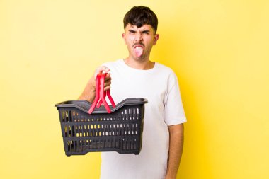 Genç İspanyol adam iğreniyor, sinirleniyor ve dili dışarı çıkıyor. boş alışveriş sepeti kavramı