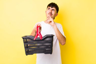 Genç İspanyol adam düşünüyor, kuşkulu ve şaşkın hissediyor. boş alışveriş sepeti kavramı