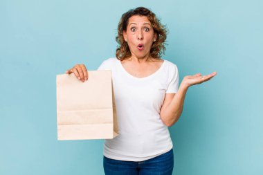 Orta yaşlı kadın şaşırmış ve şok olmuş görünüyor. Çenesi düşmüş ve elinde bir nesne var. konsepti kaldır