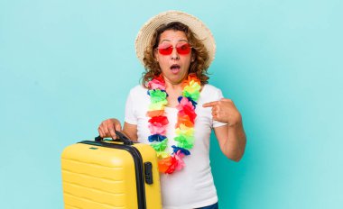 Orta yaşlı bir kadın şok olmuş ve ağzı açık, kendini işaret ederek şaşırmış görünüyor. Yaz tatili konsepti