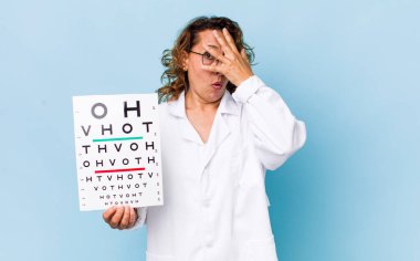 Orta yaşlı bir kadın şok olmuş, korkmuş ya da korkmuş görünüyor, yüzünü elleriyle kapatıyor. vizyon testi kavramı