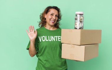 Orta yaşlı bir kadın mutlu bir şekilde gülümsüyor, el sallıyor, sizi selamlıyor ve selamlıyor. gönüllü ve bağış konsepti