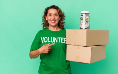 Orta yaşlı bir kadın neşeli bir şekilde gülümsüyor, mutlu hissediyor ve bir tarafı işaret ediyor. gönüllü ve bağış konsepti