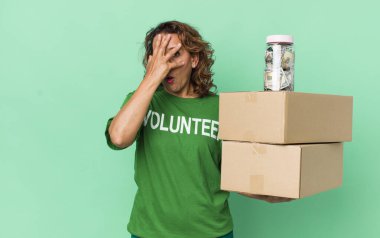 Orta yaşlı bir kadın şok olmuş, korkmuş ya da korkmuş görünüyor, yüzünü elleriyle kapatıyor. gönüllü ve bağış konsepti