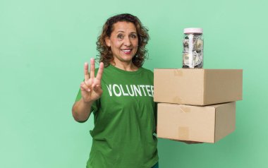 Orta yaşlı kadın gülümsüyor ve arkadaş canlısı görünüyor, üç numarayı gösteriyor. gönüllü ve bağış konsepti