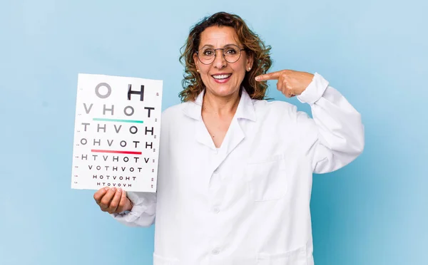 middle age woman smiling confidently pointing to own broad smile. vision test concept