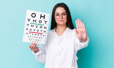 Genç bir kadın ciddi görünüyor. Avuç içini gösteriyor. Durdurma hareketi yapıyor. optik görüş testi konsepti