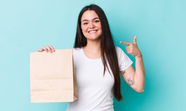 Genç, yetişkin bir kadın kendi gülüşünü işaret ederek kendine güvenerek gülümsüyor. konsepti kaldır