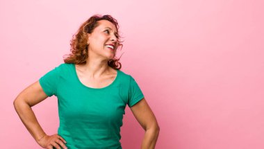 Orta yaşlı İspanyol kadın mutlu, neşeli ve kendinden emin görünüyor, gururla gülümsüyor ve iki elini de kalçasında istiyor.