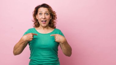 Orta yaşlı İspanyol kadın mutlu, şaşkın ve gururlu hissediyor. Heyecanlı ve şaşkın bir bakışla kendini işaret ediyor.