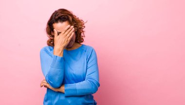Orta yaşlı İspanyol kadın stresli, utanmış ya da üzgün görünüyor, baş ağrısı var, yüzünü elle kapatıyor.