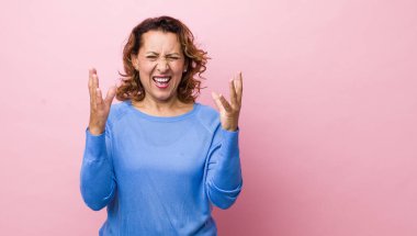 Orta yaşlı Latin bir kadın öfkeyle bağırıyor, stresli hissediyor ve ellerini havaya kaldırıp 