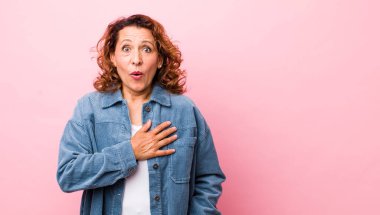 Orta yaşlı İspanyol bir kadın şok olmuş ve şaşırmış hissediyor, gülümsüyor, el ele tutuşuyor, mutlu ya da şükran duyuyor.