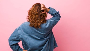 Orta yaşlı İspanyol bir kadın bilgisiz ve kafası karışık, bir çözüm düşünüyor, eli kalçasında, diğeri ise kafasında, dikiz aynasından.