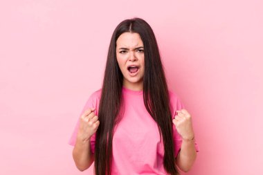 Genç yetişkin bir kadın sinirli, sinirli, kızgın bakışlar ve sıkı yumruklarla bağırıyor. Öfkeli hissediyor.