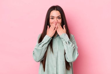 Genç yetişkin bir kadın mutlu ve heyecanlı, şaşırmış ve hayrete düşmüş elleriyle ağzını kapatmış, tatlı bir ifadeyle kıkırıyor