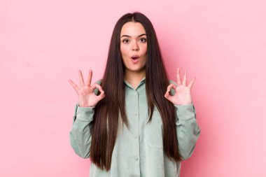 Genç bir kadın şok olmuş, şaşırmış ve şaşırmış hissediyor. İki eliyle de onay işareti yapıyor.