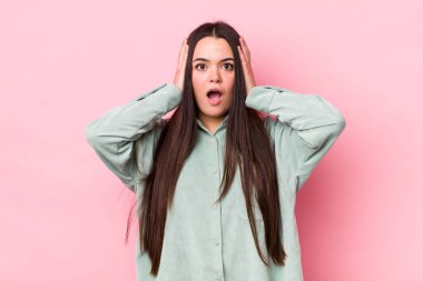 Genç bir kadın mutsuz, korkmuş ya da endişeli görünüyor, ağzı sonuna kadar açık ve iki kulağını da elleriyle kapatıyor.