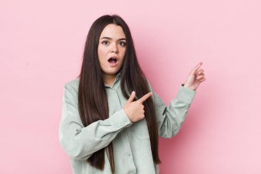 Genç bir kadın şaşkın ve şaşırmış hissediyor. Kenardaki fotokopi alanını işaret ediyor. Şaşırmış ve ağzı açık bakıyor.