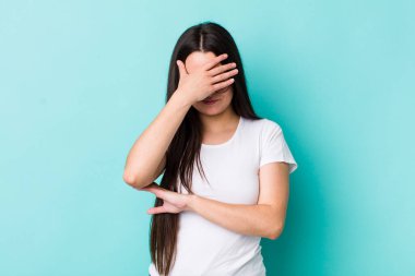 Genç bir kadın stresli, utanmış ya da üzgün görünüyor, baş ağrısı var, yüzü elle kapatılmış.