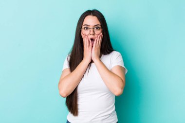 Genç bir kadın şok olmuş ve korkmuş hissediyor, ağzı açık ve elleri yanaklarında korkmuş görünüyor.