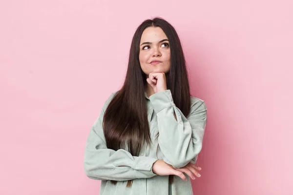 young adult woman feeling thoughtful, wondering or imagining ideas, daydreaming and looking up to copy space