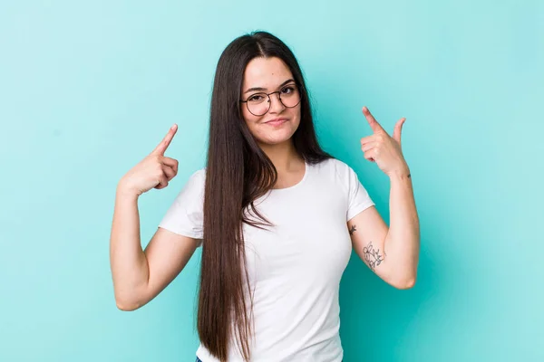 young adult woman with a bad attitude looking proud and aggressive, pointing upwards or making fun sign with hands
