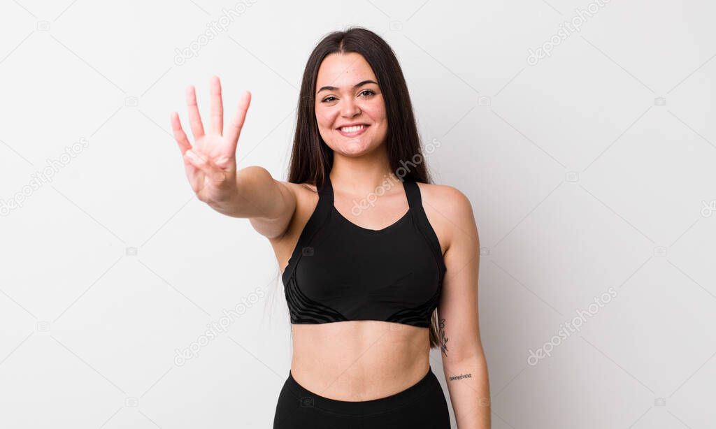 young adult woman smiling and looking friendly, showing number four. fitness concept