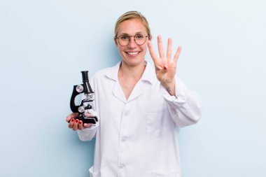 Genç sarışın kadın gülümsüyor ve arkadaş canlısı görünüyor, dört numarayı gösteriyor. Mikroskop konseptine sahip bilim adamı