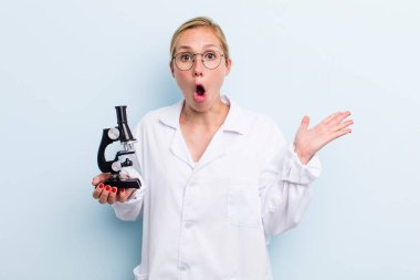Genç sarışın kadın şaşırmış ve şok olmuş görünüyor. Çenesi düşmüş ve elinde bir nesne var. Mikroskop konseptine sahip bilim adamı