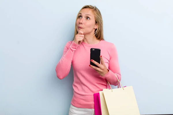 若い大人のブロンドの女性は疑って混乱してる ショッピングバッグのコンセプト — ストック写真