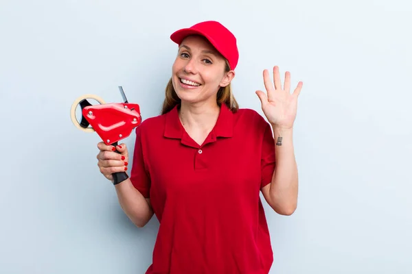 young adult blonde woman smiling happily, waving hand, welcoming and greeting you. employee concept