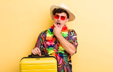 Ağzı ve gözleri sonuna kadar açık ve eli çenesinde olan yakışıklı bir genç. Yaz tatili konsepti