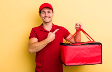 Genç yakışıklı adam neşeyle gülümsüyor, mutlu hissediyor ve bir tarafı işaret ediyor. Pizza teslimatı kavramı