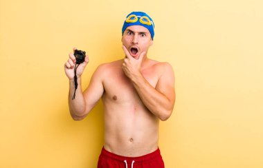 Ağzı ve gözleri sonuna kadar açık ve eli çenesinde olan yakışıklı bir genç. yüzücü kavramı