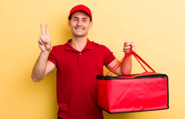 Genç yakışıklı adam gülümsüyor ve arkadaş canlısı görünüyor, iki numarayı gösteriyor. Pizza teslimatı kavramı